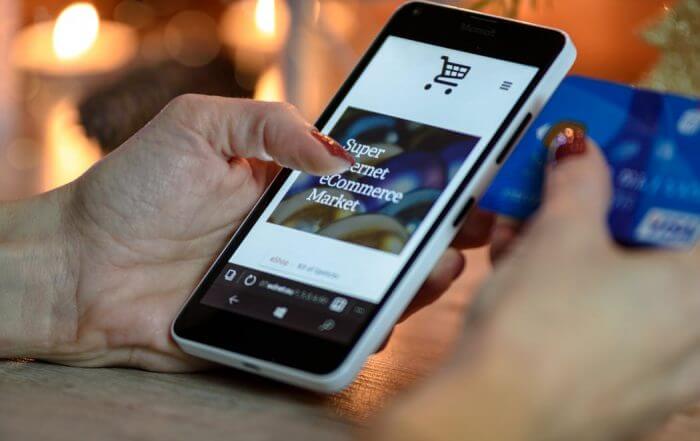 Person holding a smartphone displaying an online shopping website, with a credit card in the other hand.