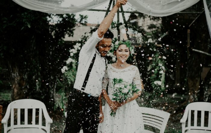 A couple celebrates under a canopy with confetti falling, surrounded by chairs and greenery.