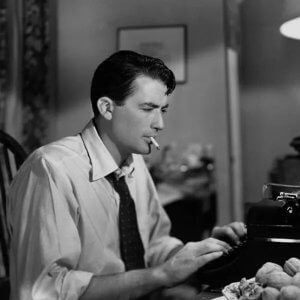 A man typing on a typewriter with a cigarette in his mouth, seated at a desk with crumpled paper.