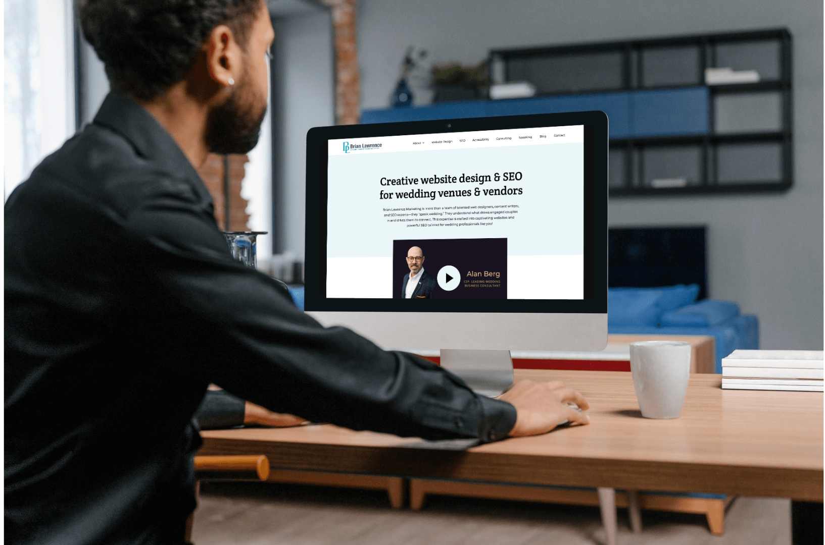 Man sitting at a desk looking at a computer screen displaying a website about creative website design and SEO for wedding venues and vendors.